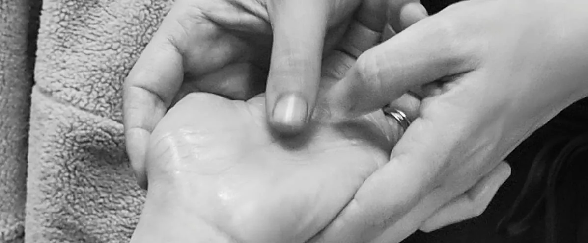 Mains posées avec douceur l'une sur l'autre, en noir et blanc, évoquant le toucher relationnel.